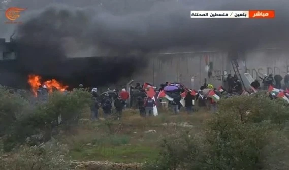 Cerca del Muro del Apartheid en Bil'in, Ramallah, los jóvenes palestinos salieron en su manifestación semanal, alzaron la bandera palestina en el muro e incendiaron llantas de goma.