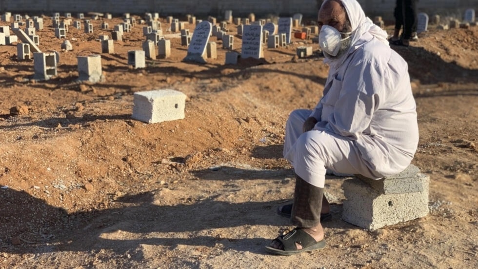 Un hombre sentado junto a las tumbas de las víctimas de las inundaciones repentinas en Derna.