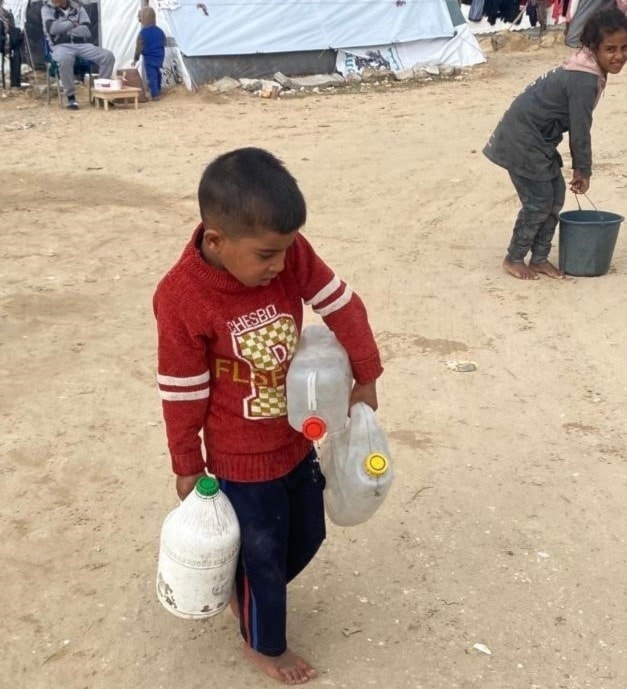 Hamza Musabih, de seis años, camina descalzo y apenas puede cargar los tres galones de agua potable que carga para su familia. 