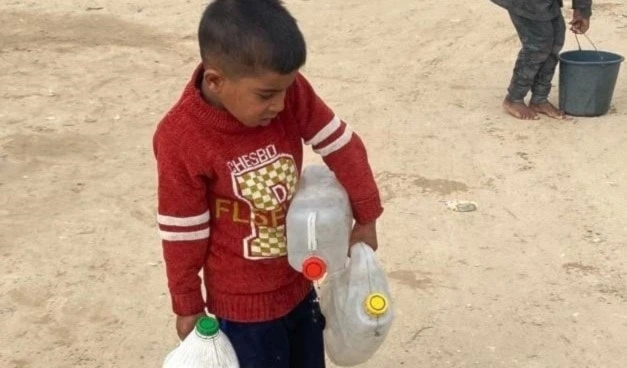 Hamza Musabih, de seis años, camina descalzo y apenas puede cargar los tres galones de agua potable que carga para su familia.