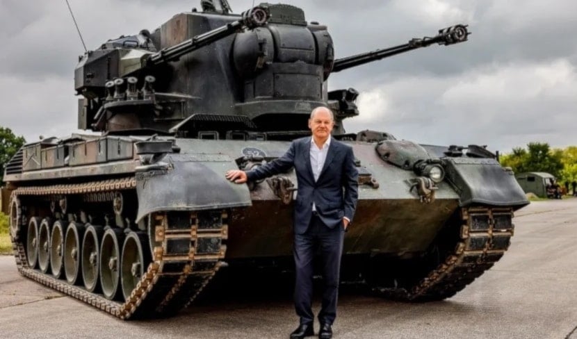 El canciller alemán Olaf Scholz posa frente a un tanque de guerra.