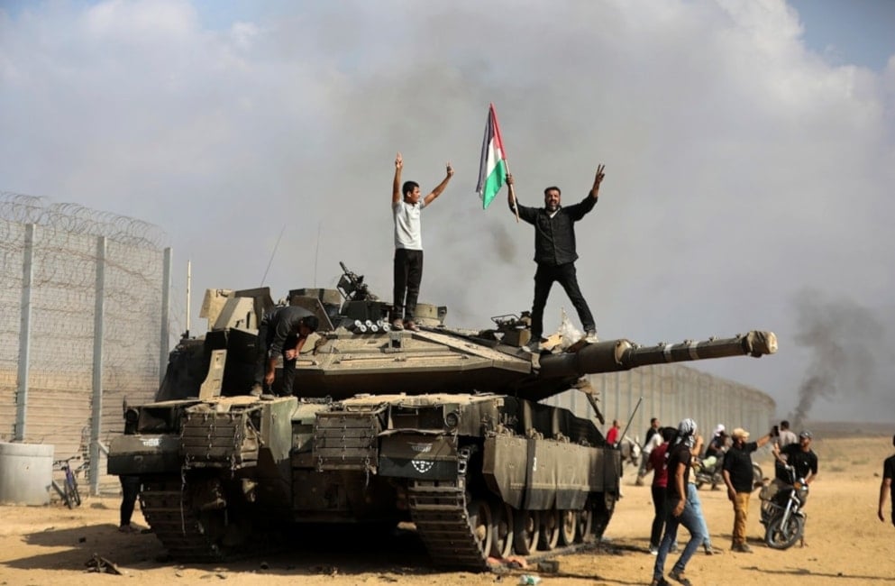 Palestinos ondean su bandera y celebran en un tanque israelí destruido en la valla de la Franja de Gaza al este de Khan Yunis, durante los eventos del 7 de octubre de 2023. 