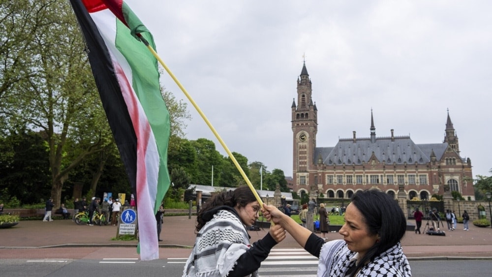 Dos manifestantes izando la bandera de Palestina ocupada frente al Palacio de la Paz, sede de la CIJ, en La Haya. (Foto: AP)