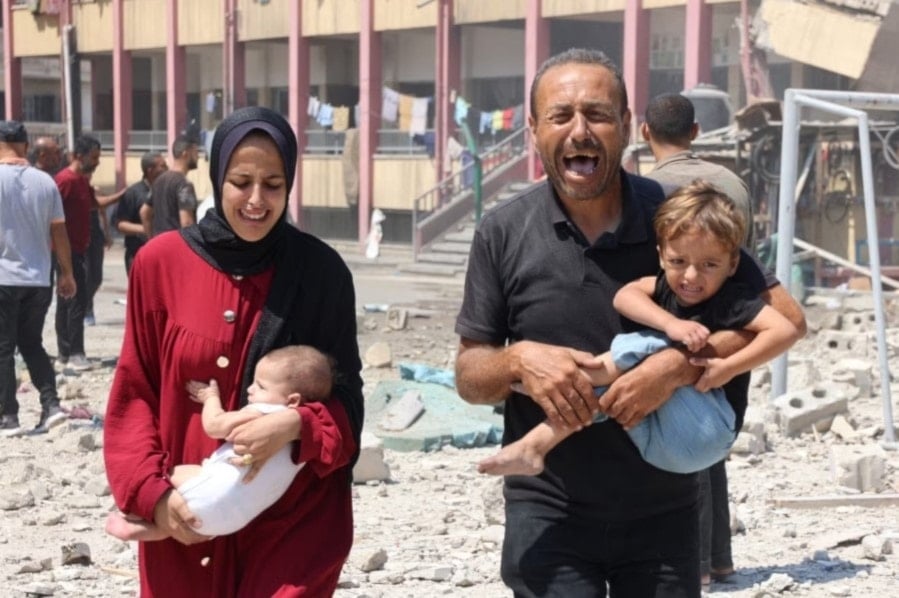 Una familia palestina carga a sus hijos mientras huye tras un ataque israelí a una escuela que alberga a desplazados en el barrio de Al-Rimal. Foto: AFP