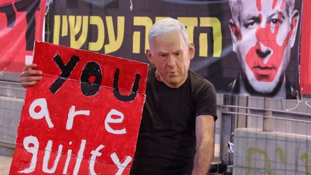 Manifestante con una máscara que representa al jefe del gobierno de ocupación, Benjamín Netanyahu, levanta una pancarta: “Eres culpable”, durante las manifestaciones. 31 de agosto de 2024 (Foto: FP)