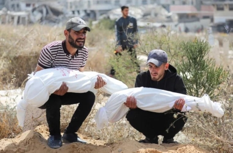 Dos palestinos cargan cuerpos de niños mártires en ataques aéreos israelíes contra Gaza. 28 de mayo de 2025 (Foto: Reuters)