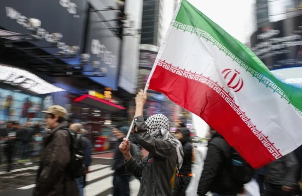 Hombre porta bandera iraní durante manifestación contra la guerra en Nueva York.