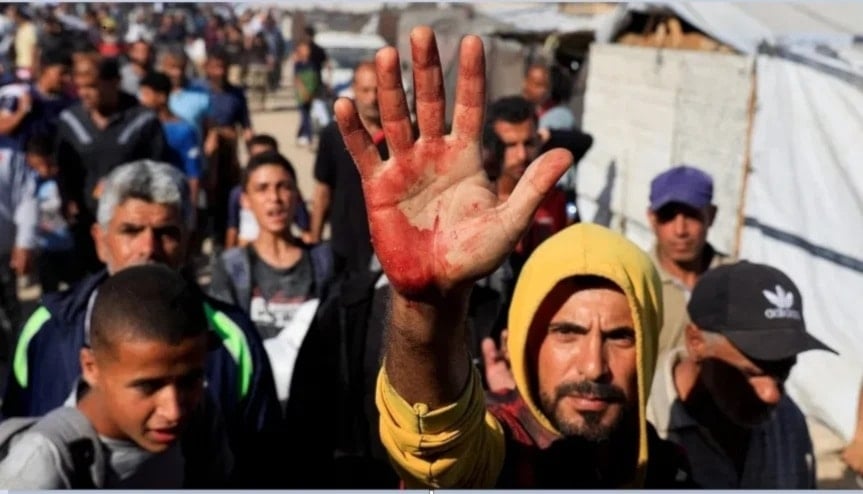 Palestino levanta su mano ensangrentada tras cargar a personas heridas por el fuego israelí en Khan Yunis.