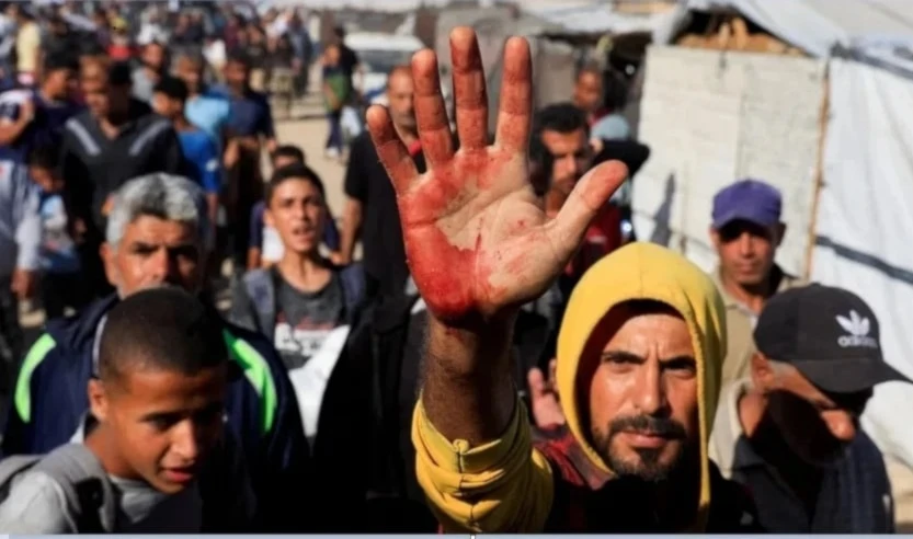 Palestino levanta su mano ensangrentada tras cargar a personas heridas por el fuego israelí en Khan Yunis.