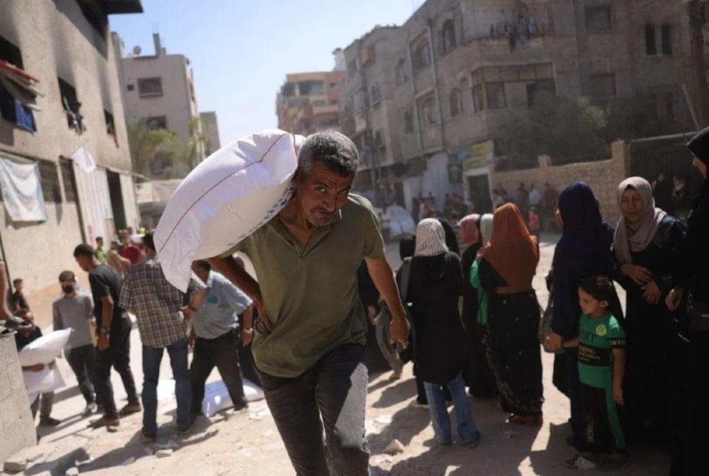 Hombre palestino carga un saco de harina, mientras otros esperan en centros de distribución en Gaza.